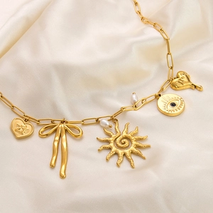 Detail of 18K gold charm bracelet with heart, sun, and evil eye on paperclip chain