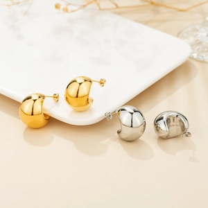Detailed view of chunky C-shaped gold and silver earrings on a marble display board