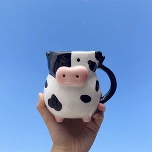 Person holding 20oz ceramic cow shaped 3D coffee mug against a bright blue sky background