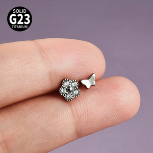Vue macro détaillée de la boucle d'oreille en titane G23 fleur et papillon sur les doigts