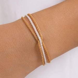 Detailed view of layered gold and silver textured chain bracelets on a female wrist