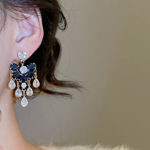 Close-up of dangling zircon earrings with blue flowers and sparkling water-drop tassels