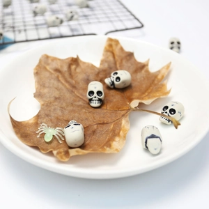 Miniature Halloween skull and spider decorations arranged on a ceramic plate with maple leaf