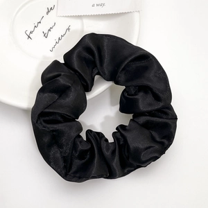Elegant black satin scrunchie with silky texture on minimalist white decorative plate