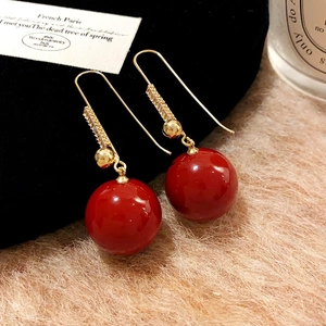 Detail of gold zircon earrings featuring a large glossy red bead on soft background