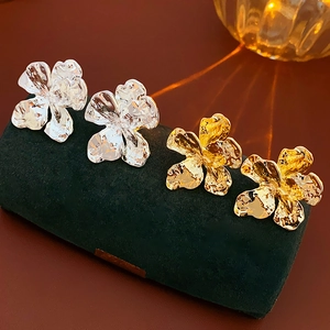 Close-up of gold and silver metallic flower earrings with textured petals on velvet