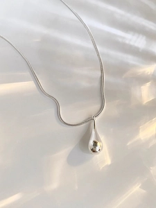 Macro shot of minimalist silver teardrop pendant on high-polished snake chain necklace
