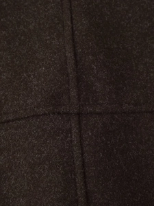 Detailed macro view of dark brown wool coat fabric featuring durable cross-stitched seams