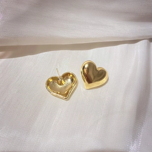 Vue détaillée de boucles d'oreilles cœur 3D en métal doré sur soie blanche brillante