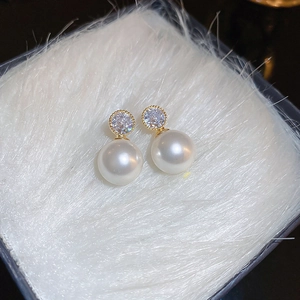 Macro detail of gold plated pearl earrings with zircon stones on white plush background