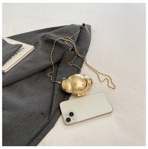 Mini golden metal shell bag with pearl chain strap styled next to a smart phone
