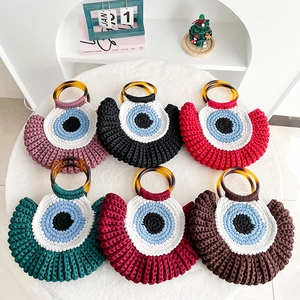 Handwoven evil eye handbags in six colors with amber handles on a minimalist white desk