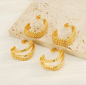 Detail of gold layered rope texture C-shaped hoop earrings on natural stone background