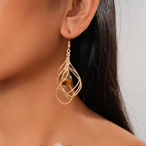 Detail view of twisted gold rhombus earrings with tiger eye stone on a model profile