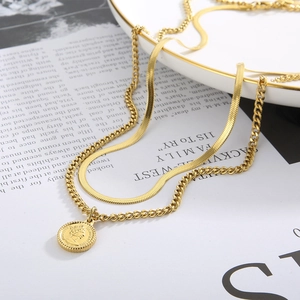 Detail of layered gold snake and cuban chain necklace with coin pendant on white plate