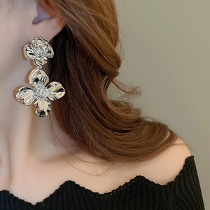 Detail of silver oversized flower earrings with metallic texture worn by a model