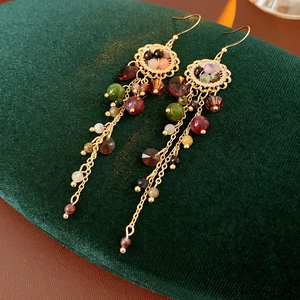 Macro shot of bohemian gold tassel earrings with colorful crystals on green velvet