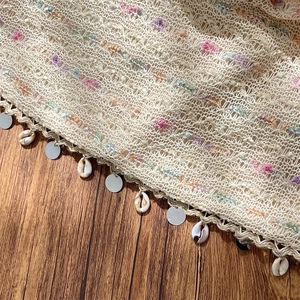 Detail of beige crochet knit bag with colorful sequins, shell charms, and tassel trim