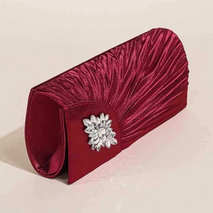 Detailaufnahme der weinroten Satin-Clutch mit Plisseefalten und funkelnder Kristallbrosche