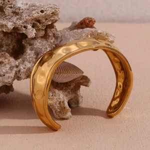 Detail shot of a minimalist 18K gold-plated cuff bracelet with a hammered wave texture