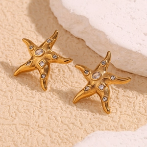 Detailed close-up of gold starfish earrings with sparkling zircon stones on white rock