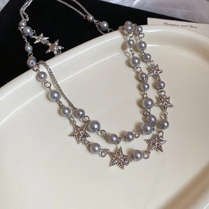 Detail of double-layered beaded necklace with silver star pendants on white tray