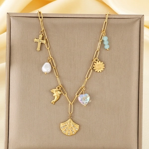 Detail of gold charms necklace with shell, pearl, cross, and dolphin pendants on chain