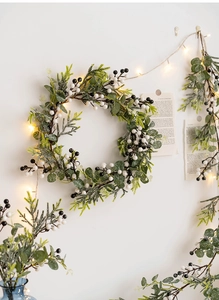 Close-up of frosted Christmas wreath with LED lights and white berries on white wall