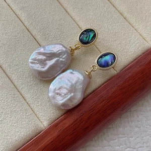 Macro shot of baroque pearl earrings with iridescent blue gemstones on beige velvet