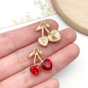 Detail of red heart crystal cherry charms and gold textured fruit pendants in hand