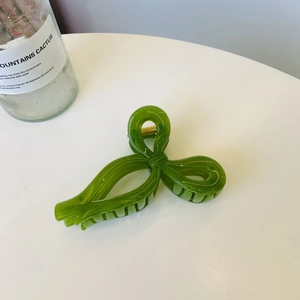 Detail of green ribbon bow hair claw clip with golden metal spring on white surface