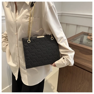Detail of geometric quilted leather texture on a black tote with gold chain strap