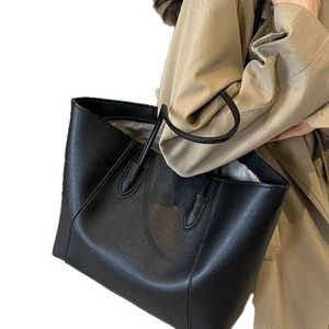 Minimalist black large capacity tote bag shown on model with sleek faux leather texture