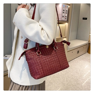 Détail d'un sac cabas tressé bordeaux montrant la texture du cuir et finitions dorées
