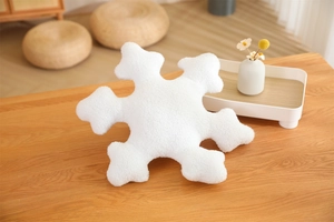 Detailed view of a white snowflake plush pillow on a wooden table in a minimalist home setting