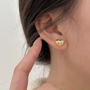 Macro view of gold-plated silver heart stud earring with bow detail on female model