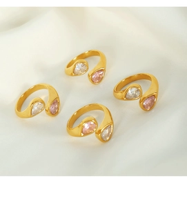 Macro shot of four 18k gold plated teardrop white and pink zircon rings on white silk fabric