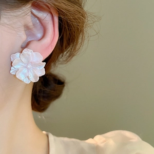 Close-up of pearlescent floral earrings with layered 3D petals worn by a model