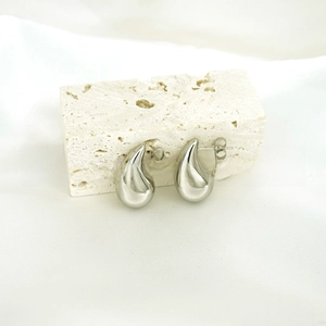Polished silver teardrop earrings resting on a white stone textured background