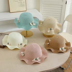 Détail de chapeaux de paille colorés pour enfants avec bord ondulé et nœuds cerise