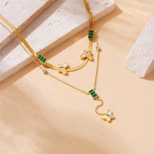 Detailed macro view of layered gold stainless steel necklace with green gems and butterfly charms