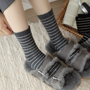 Women's warm gray striped wool socks paired with cozy plush slippers in a home setting