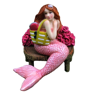 Resin mermaid figurine with red hair and pink fish tail sitting on rose background