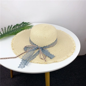 Detail of a beige wide-brim straw hat with frayed edges and a lace-trimmed ribbon bow