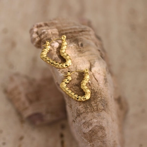 Close-up of golden heart-shaped earrings with irregular hammered texture and metallic luster