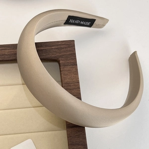 Detail of a beige satin headband with a thick profile and handmade inner label