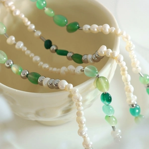 Collana artigianale in perle d'acqua dolce e pietre verdi su una tazza in porcellana bianca