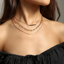 Close-up of triple-layered golden necklace set featuring a long bar pendant on fine chain