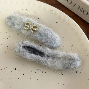 Close-up of grey plush hair clips with rhinestone bow on a ceramic plate for women