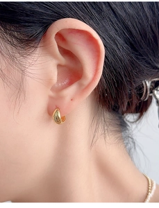 Close-up of elegant gold drop earrings worn on ear showing polished metallic finish